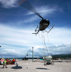 Figure 1: Helicopter and bait-spreading bucket undertaking the first aerial eradication operation in the south Pacific, on the Aleipata Islands, Samoa (Photo; Stuart Chape, SPREP).